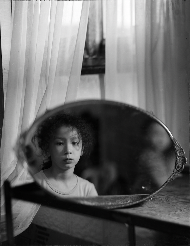 Black and white photo of a young Asian child looking into a mirror.